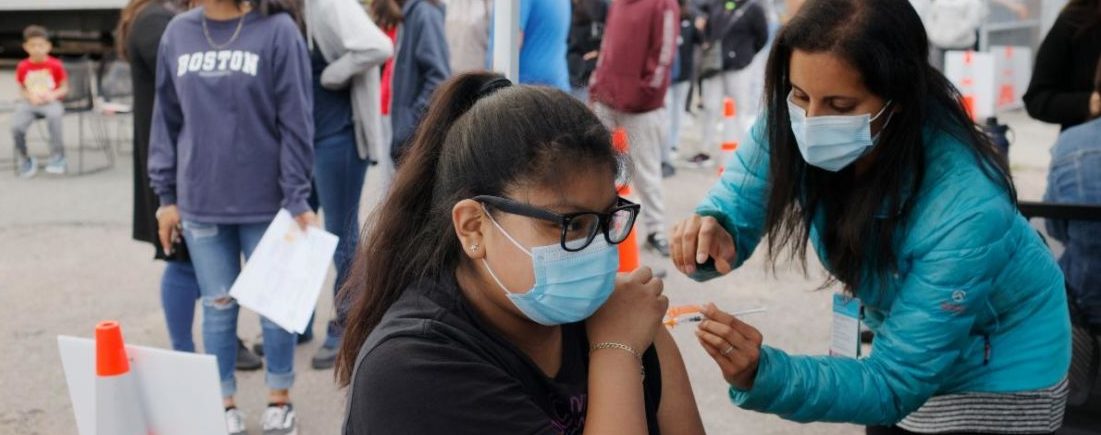 a masked individual administering a vaccine to another masked individual