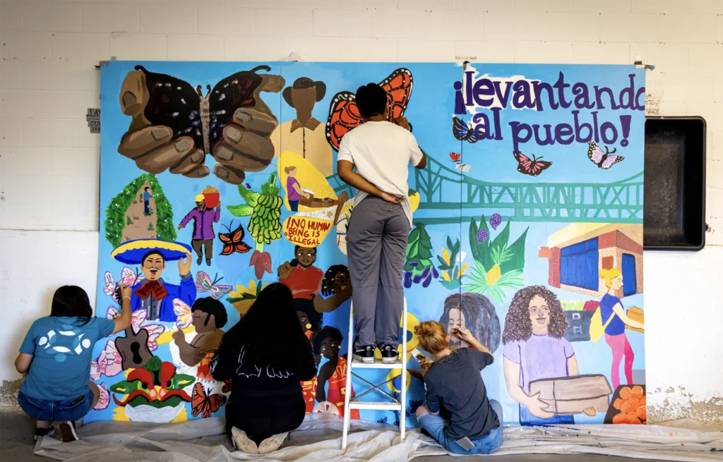 People painting a mural that says "Levantando al pueblo"